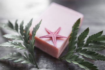 Handmade soap, starfish and green leaves on a wooden background