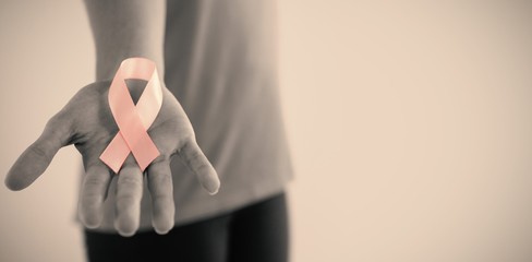 Mid section of woman holding pink breast cancer awareness ribbon