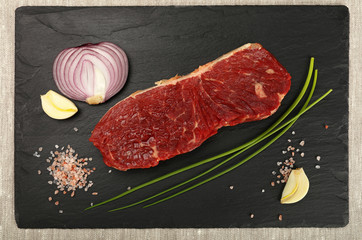 Raw beef steak meat cut and spices on black board