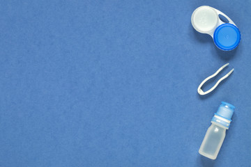 Accessories for contact lenses: container, solution, tweezers. Blue background.