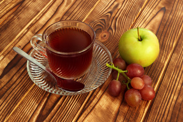 Hot tea in glass cup with apple and grapes on wooden table planks