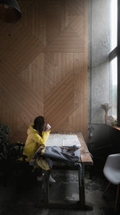 Fototapeta premium Beautiful Caucasian female millennial hiker tourist in a yellow raincoat studying a map in a rustic lodge