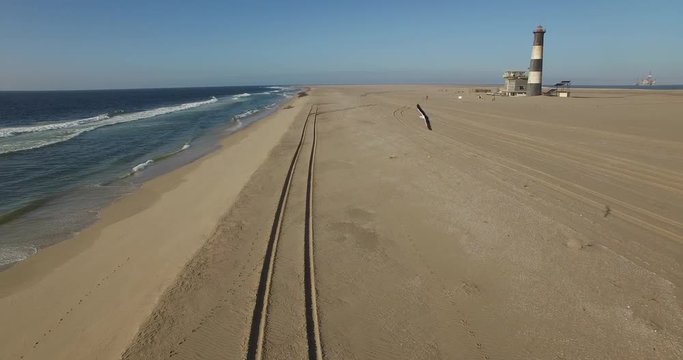 Aerial view footage of desert sand peninsula, old lighthouse and power station building on ocean seals beach, Walvis Bay lagoon view with sea background and ships at Namibia's Atlantic west coast