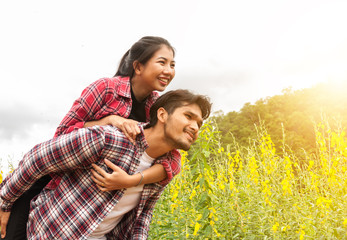 Handsome man Smiling and woman riding piggyback on man shoulders. Happy young couple having fun together his girlfriend around the field outdoor, travel in holiday on summer,concept of romance