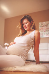 Pregnant brunette woman touching her belly and sitting on floor.