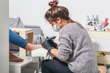 A young white manicurist girl makes a pedicure electric nail drill machine to the client in the...