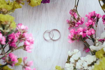 Close-up view of golden wedding rings and beautiful small flowers on wooden tabletop