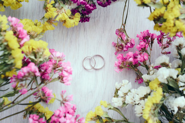 Close-up view of golden wedding rings and beautiful small flowers on wooden tabletop