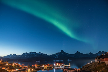 Seaside village with green aurora at twilight on the coast of Greenland