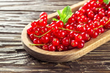 Ripe redcurrants in a wooden plate on a wooden background.