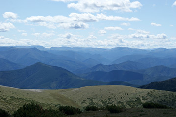 Fototapeta premium A mountain landscape shot from one of the peaks. Blue mountains to the horizon and the sky with clouds. Chamar-Daban (Khamar-Daban) montains, Siberia, Russia. Summer, day.