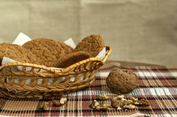 A walnut, walnut kernels ahd small basket of oatmeal cookies on a colored tablecloth close-up.
