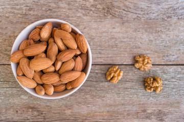 White ceramic bowl with almond and three walnuts on the wooden background