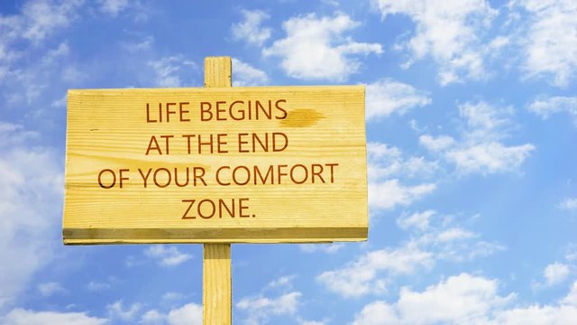 Motivational quote to create future. Life begins at the end of your comfort zone. Words on a wooden sign against time lapse clouds in the blue sky.