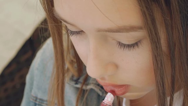 Pretty female teen applying the lipstick on the lips. Slowly