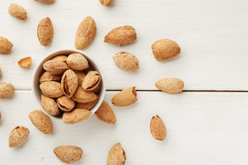 Almond in shell in a white bowl on a wooden table, top view