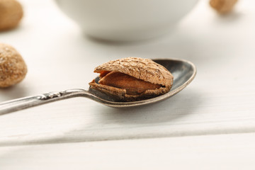 Metal spoon with almond in shell in it on a white wooden table, selective focus