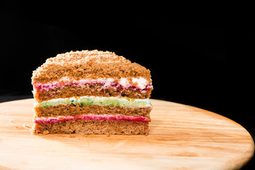 Close-up of sweet homemade layered honey cake on round wooden board on dark background. Cake made with different in color layer of sour cream