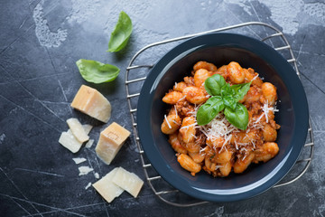 Plate of italian potato gnocchi with meat sauce and cheese, top view on a dark grey stone background