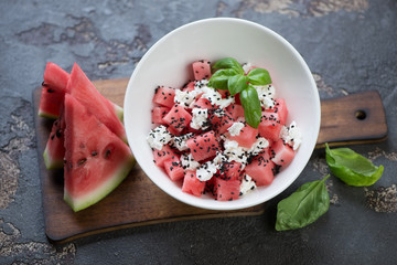 Salad with watermelon, feta cheese and black sesame served in a white bowl on a brown stone background, studio shot