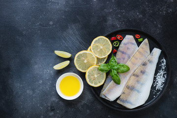 Raw fresh sudak fish with lemon, olive oil and sea salt on a dark scratched metal background, above view with space