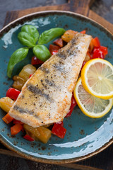 Turquoise plate with roasted sudak fish served on sauteed vegetables, closeup, studio shot