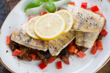 Close-up of roasted sudak fillet with vegetable saute and lemon, selective focus
