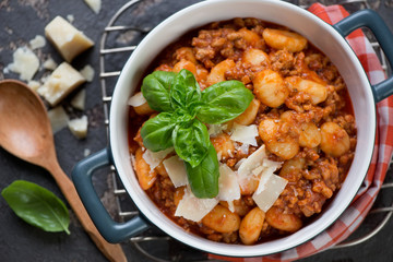 Potato gnocchi with meat sauce topped with parmesan and fresh green basil, view from above
