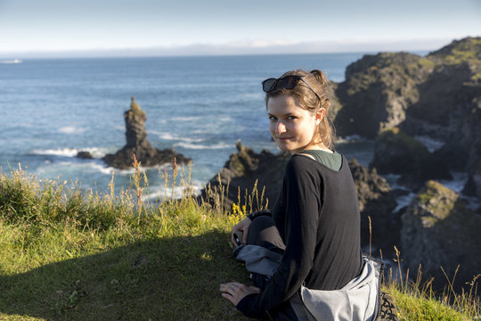 young woman near Londrangar, rock lava formation in the sea. Eroded basalt cliffs in the wild sea at coastline on Sneafellsnes peninsula, Iceland