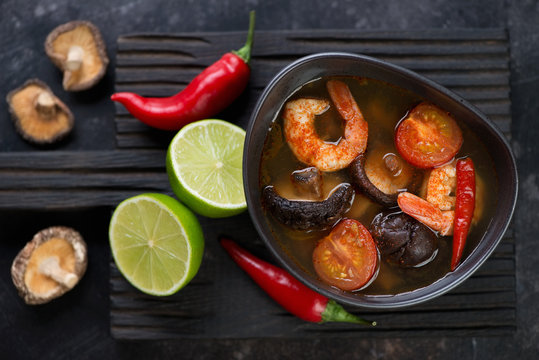 Thai hot Tom Yum soup on a black wooden serving board, flat-lay, horizontal shot