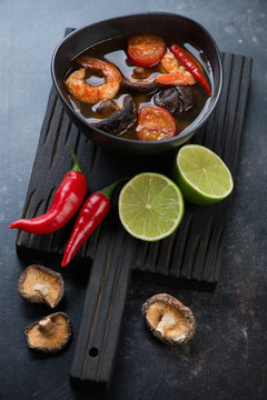Bowl of thai Tom Yum soup on a black wooden serving board, selective focus
