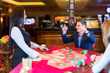 Fototapeta premium Cute lady casino dealer at poker table. Happy couple is playing Black Jack.