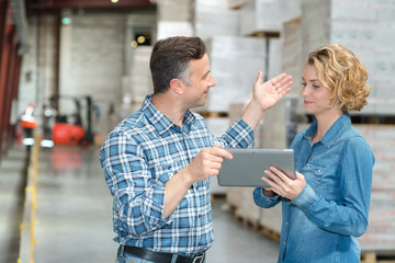 warehouse manager and worker looking at tablet in warehouse - Powered by Adobe