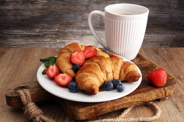 Delicious breakfast with fresh croissants, coffee and ripe berries on old wooden background
