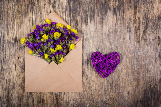 Wicker heart and wild flowers in an envelope. Romantic concept.