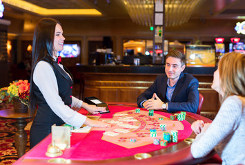 Fototapeta premium Cute lady casino dealer at poker table. Happy couple is playing Black Jack.