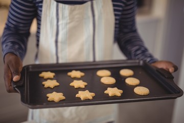 Man holding tray of cookies in kitchen