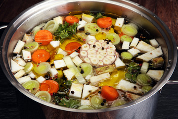 Broth with carrots, onions various fresh vegetables in a pot - colorful fresh clear spring soup. Rural kitchen scenery vegetarian bouillon or stock