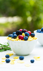 A useful breakfast in the garden on a white table. Forest berries and corn flakes.