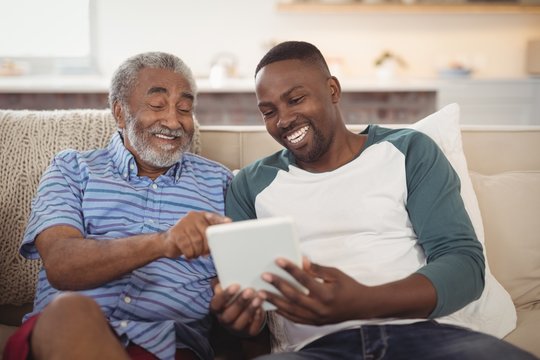 Smiling afro-american father and son using digital tablet in living room