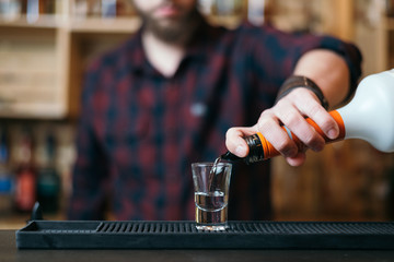Fototapeta na wymiar Handsome bearded barman is making cocktail in night club. Selective focus on glass.