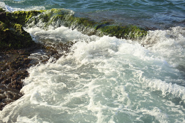 Beautiful sea wave background with green rock shore and foam near the seashore. Contrast color portrait