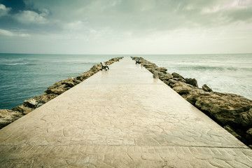 Fototapeta na wymiar Stone walkway in the sea with benches and stormy clouds in the sky. Sicily