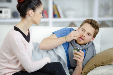 Fototapeta premium young man with cold lying on couch girlfriend taking care