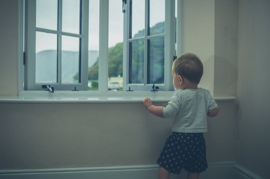 Little baby standing by window of country house