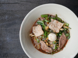 thai noddle of jumbo pork ball, pig liver, pork slide and vegetable on wooden table, hot noodle with blood pink for soup, in Thailand call Boat Noddle.