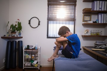 Side view of boy sitting on bed in pain