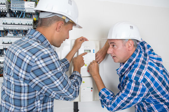 male technicians examining fusebox and thermostat