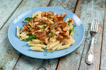 Italian penne pasta with forest chanterelle mushrooms with vintage fork on old shabby turquoise table