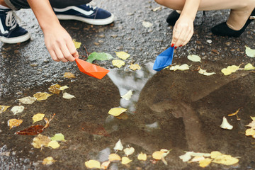 a pair of lovers lets paper boats into a puddle